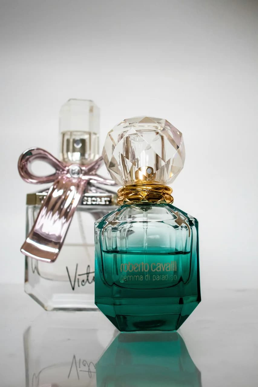 Roberto Cavalli teal Gemma di Paradiso bottle beside Victoria's Secret pink-bow bottle — dupe comparison still life