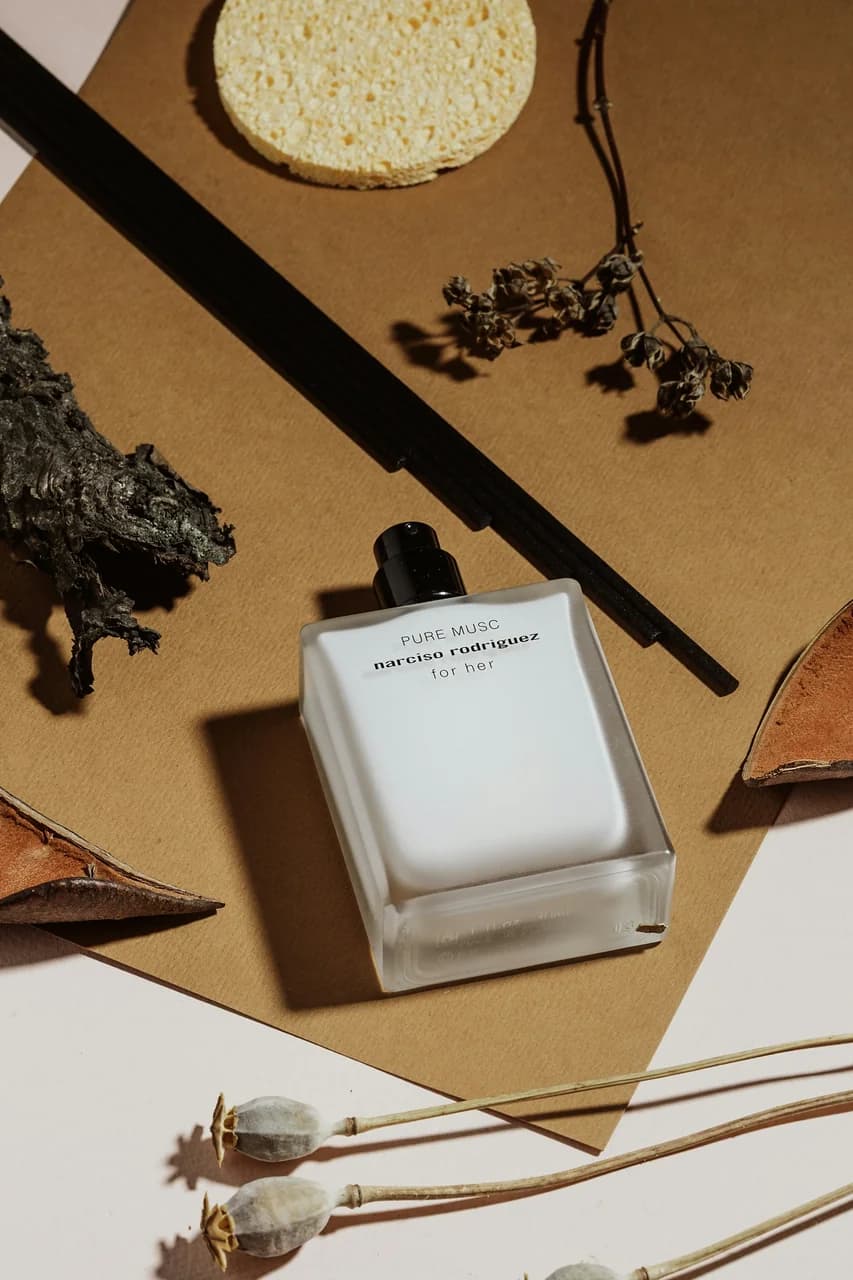 Editorial perfume bottle on a warm wood table in natural light — Kate Laine (Unsplash)