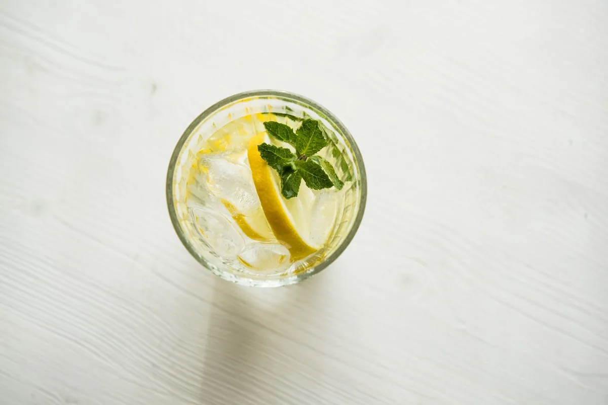 Glass of water with lemon slices and mint on white linen — clean fresh scent still life