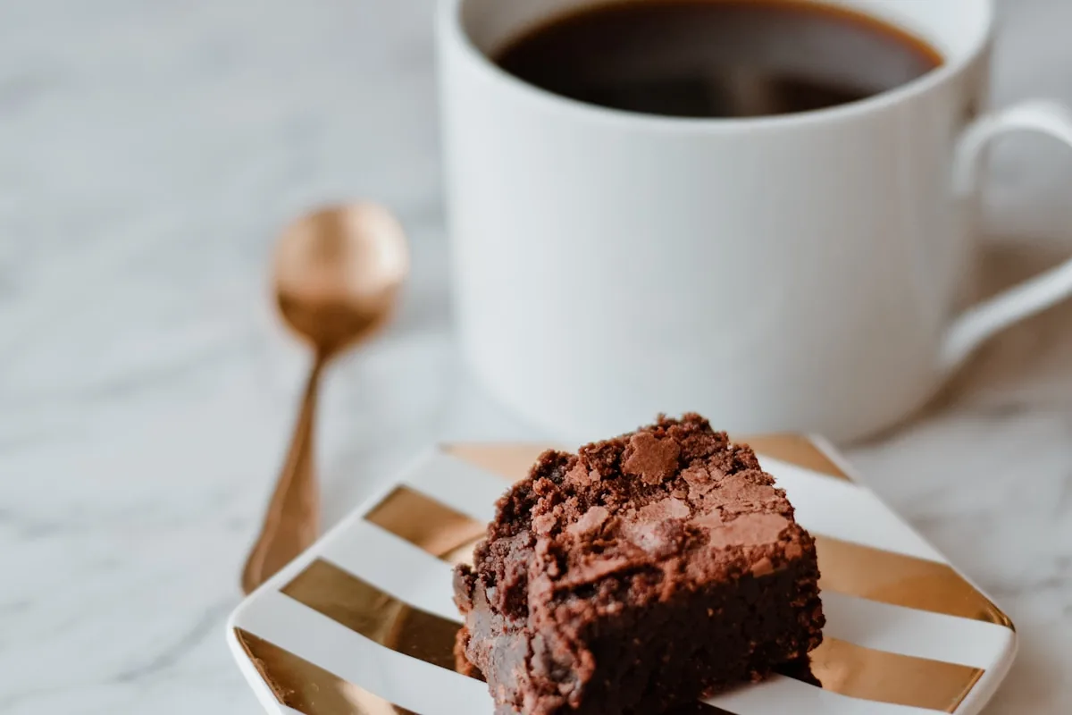 Chocolate brownie beside a cup of coffee on white — gourmand still life