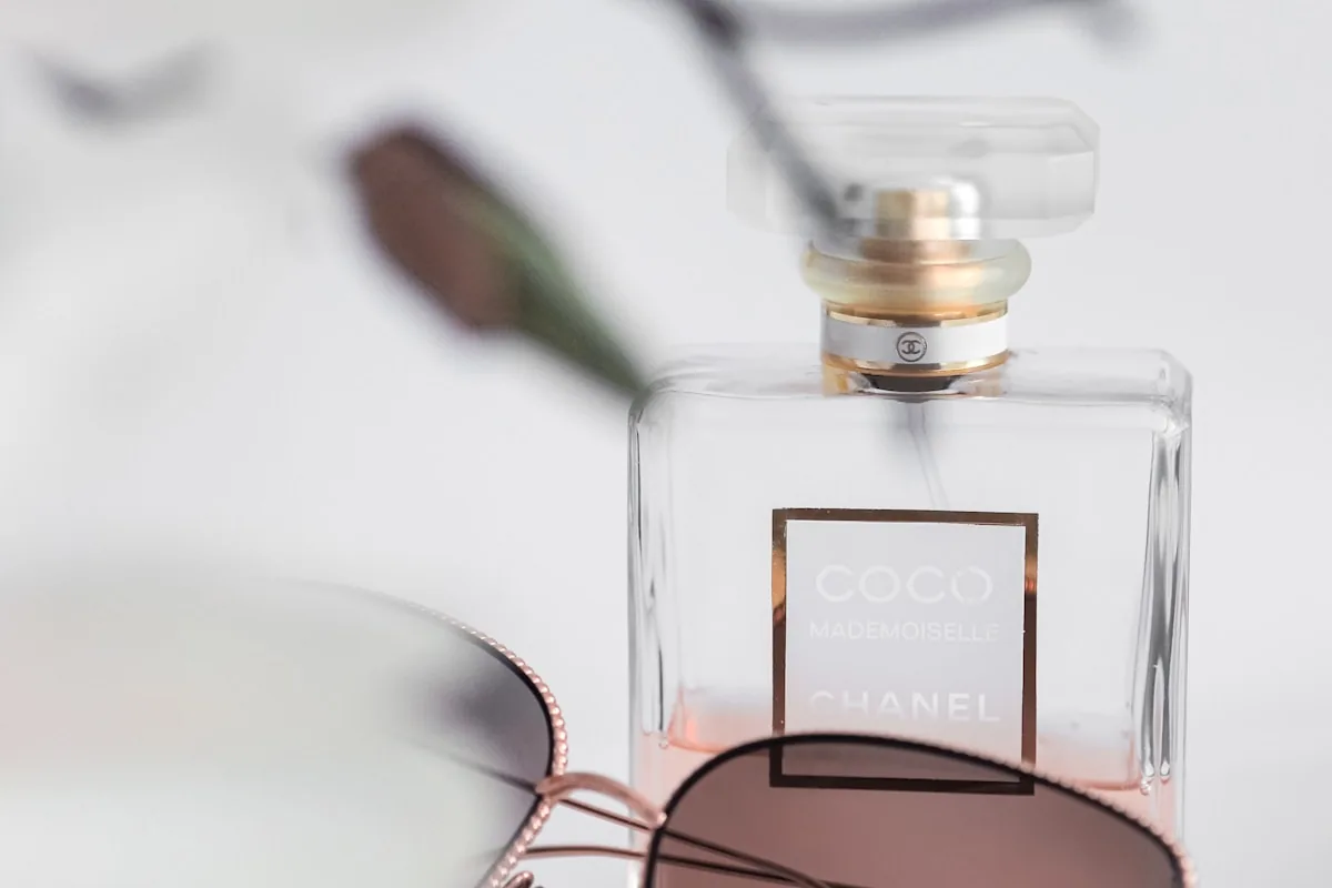 Chanel Coco Mademoiselle bottle with wire-frame rose-gold sunglasses on bright white — summer heat editorial