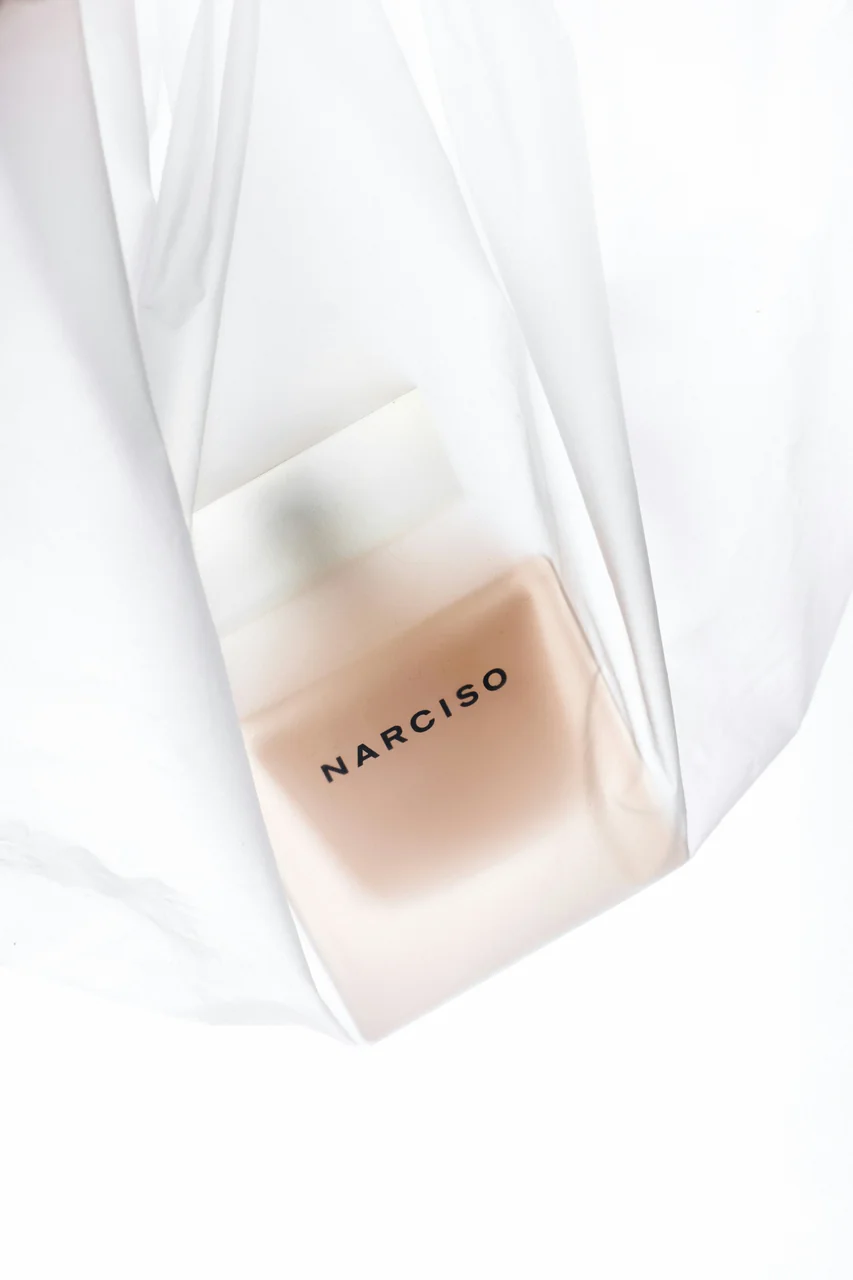 Narciso Rodriguez bottle inside a crinkled translucent plastic shopping bag on white — niche starter mood